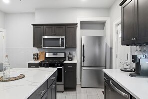 A modern kitchen with dark cabinets, a stainless steel refrigerator, a microwave, and a stove. - Skyline Chic Walk to Mt Wash Views (Pittsburgh)