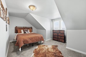 A bedroom with a sloped ceiling, a bed with a brown quilt, a wooden headboard, a cowhide rug, and a dresser with drawers. - Skyline Chic Walk to Mt Wash Views (Pittsburgh)