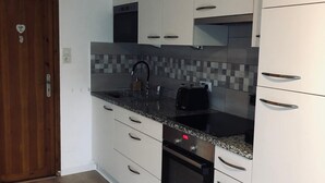 Een moderne keuken met witte kasten, een granieten werkblad, een inbouwoven en een betegelde spatwand.