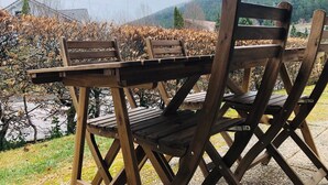 Een houten tafel en stoelen staan buiten, met uitzicht op een wijngaard en heuvels.