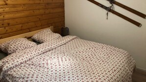 Een slaapkamer met een houten lattenplafond, een bed met bloemenbeddelsels, en ski's aan de muur.