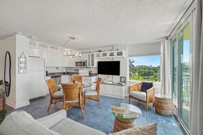 A modern kitchen with white cabinets, a dining area with wicker chairs, a glass coffee table, and a sofa. - Sunset Gulf‑Front Condo  Modern Coastal Interior, Steps to Sand (Fort Myers Beach)