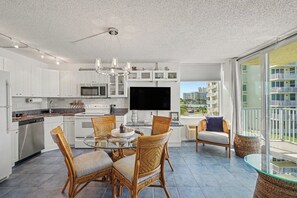 A modern kitchen with white cabinets, a built-in microwave, and a dining area with wicker chairs and a glass table. - Sunset Gulf‑Front Condo  Modern Coastal Interior, Steps to Sand (Fort Myers Beach)