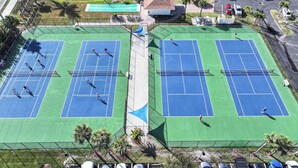 Due campi da tennis con un piccolo stagno e un edificio sullo sfondo.