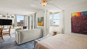 Una camera d'albergo moderna con un grande letto, un divano, una zona pranzo con TV e un balcone con vista.