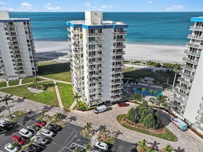A high-rise hotel with multiple balconies, a swimming pool, and a parking area. - Sunset Gulf‑Front Condo  Modern Coastal Interior, Steps to Sand (Fort Myers Beach)