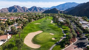 Un campo de golf con un fairway sinuoso, búnkeres de arena y un club house.