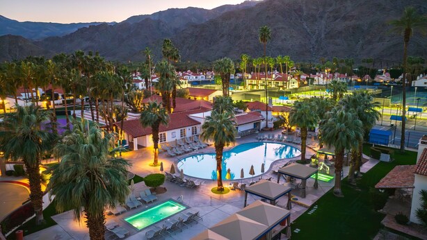 Un resort con una piscina grande, palmeras y vistas a la montaña.