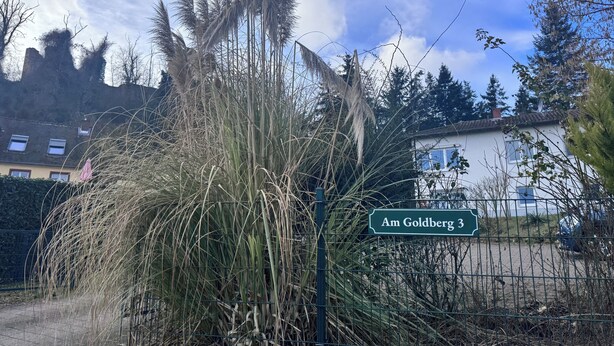 A sign reading "Am Goldberg 3" in front of a building with a fence and tall grass. - Modern vacation apartment "Am Goldberg" (Neuleiningen)