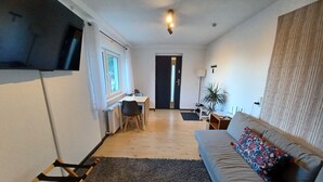 A compact living space with a kitchenette, a sofa, a desk, and a chair. - Modern vacation apartment "Am Goldberg" (Neuleiningen)