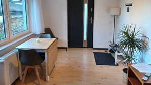 A room with a wooden floor, a table with chairs, a black door, a radiator, a window with a view, and a potted plant. - Modern vacation apartment "Am Goldberg" (Neuleiningen)