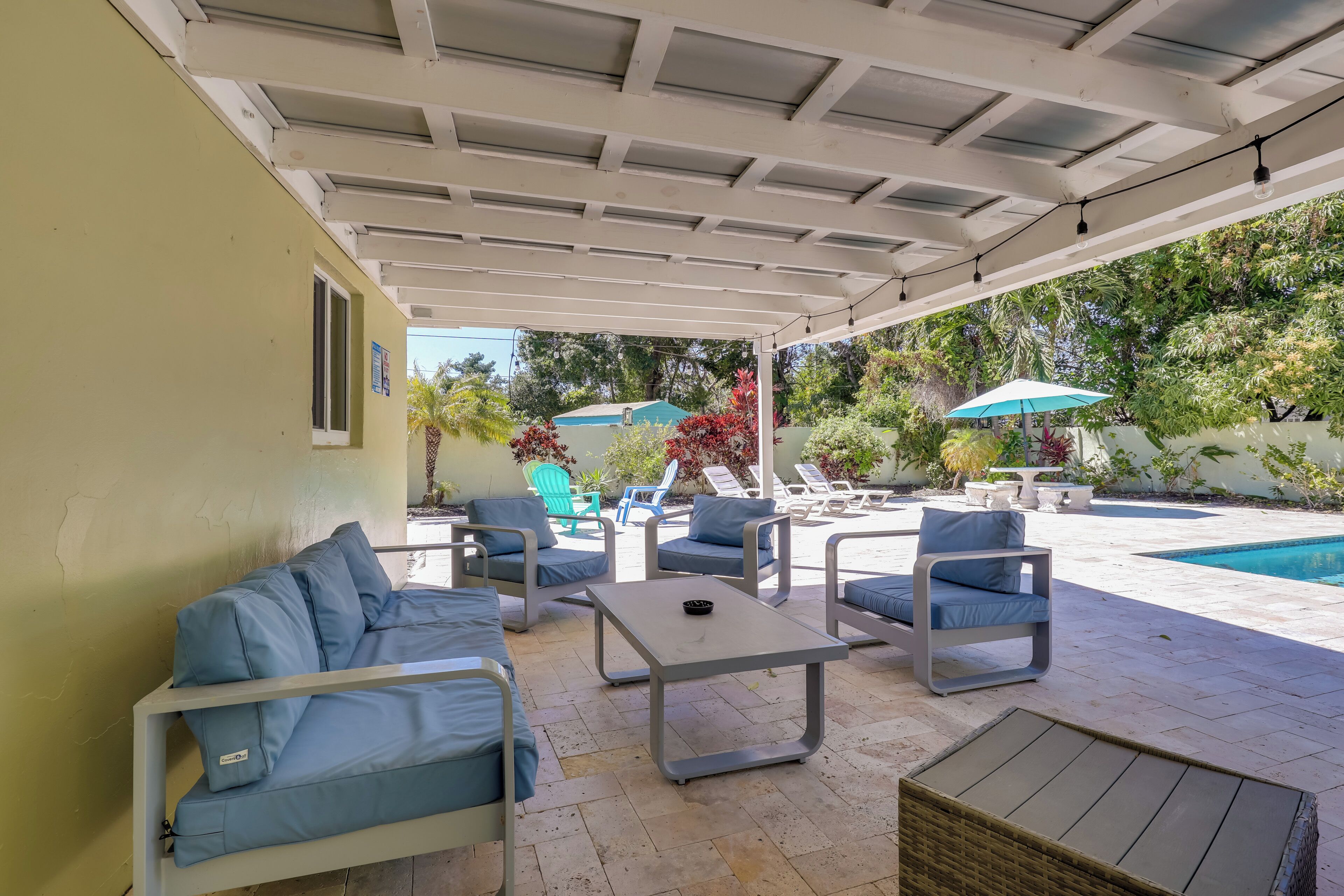A covered outdoor seating area with a pool, lounge chairs, and umbrellas.