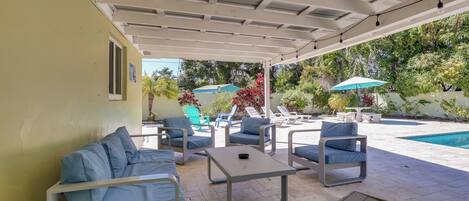 A covered outdoor seating area with a pool, lounge chairs, and umbrellas.
