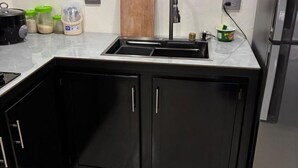 Eine Küche mit schwarzem Arbeitsplatz, einer Spüle und Schränken. Auf der Arbeitsfläche befinden sich diverse Küchenutensilien, darunter ein Topf, Gläser und ein Schneidebrett.