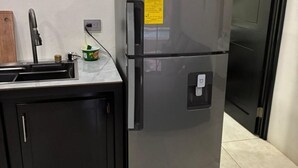 Ein Edelstahl-Kühlschrank mit Wasserspender, eine kleine Küchenarbeitsfläche mit Spüle und ein Holzschneidebrett.