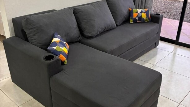 Ein dunkelgraues Sofa mit farbenfrohem geometrischem Kissen und einer schwarzen Armlehne.