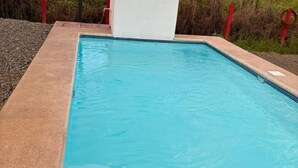 Ein rechteckiger Swimmingpool mit klarem, blauen Wasser, umgeben von einer Betonplattform und roten Sicherheitsgeländern.