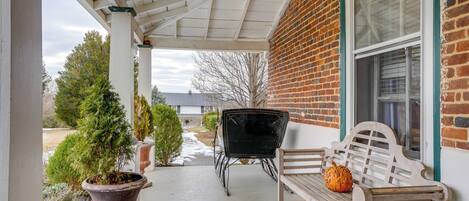 A covered porch with a bench and a planter, a brick building, and a window.