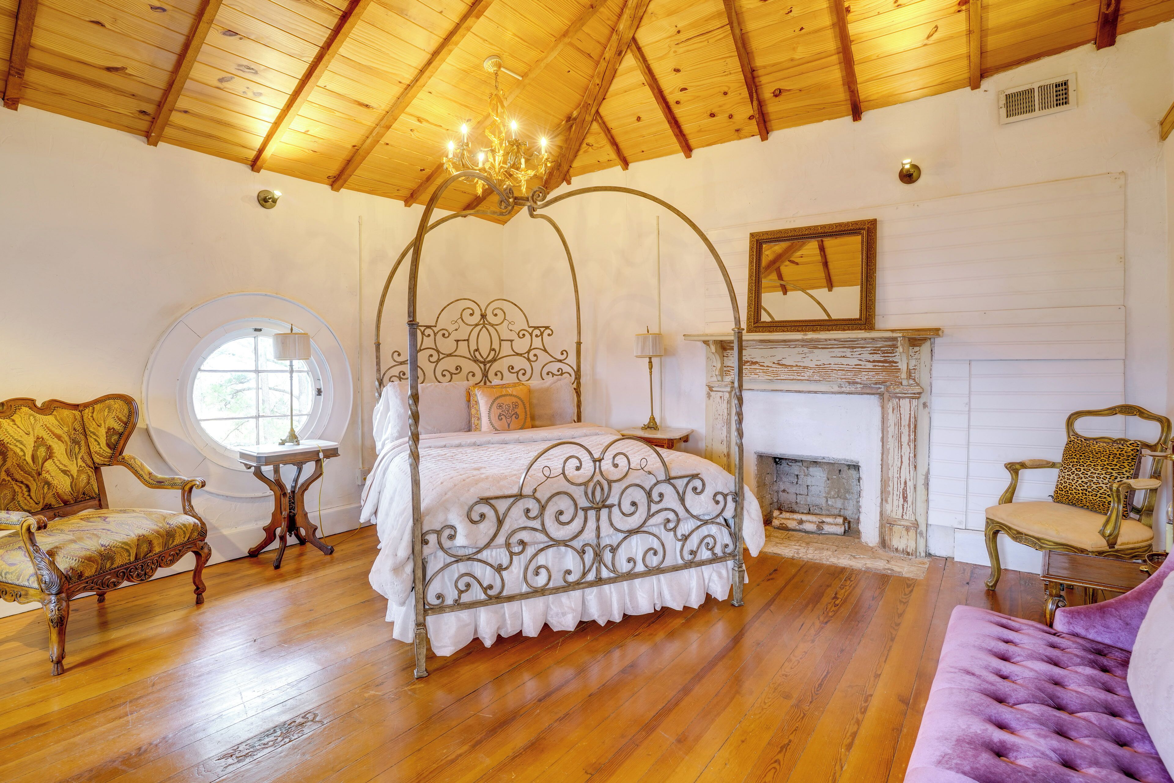 Quarto com cama de dossel, piso de madeira, lareira e mobiliário antigo.