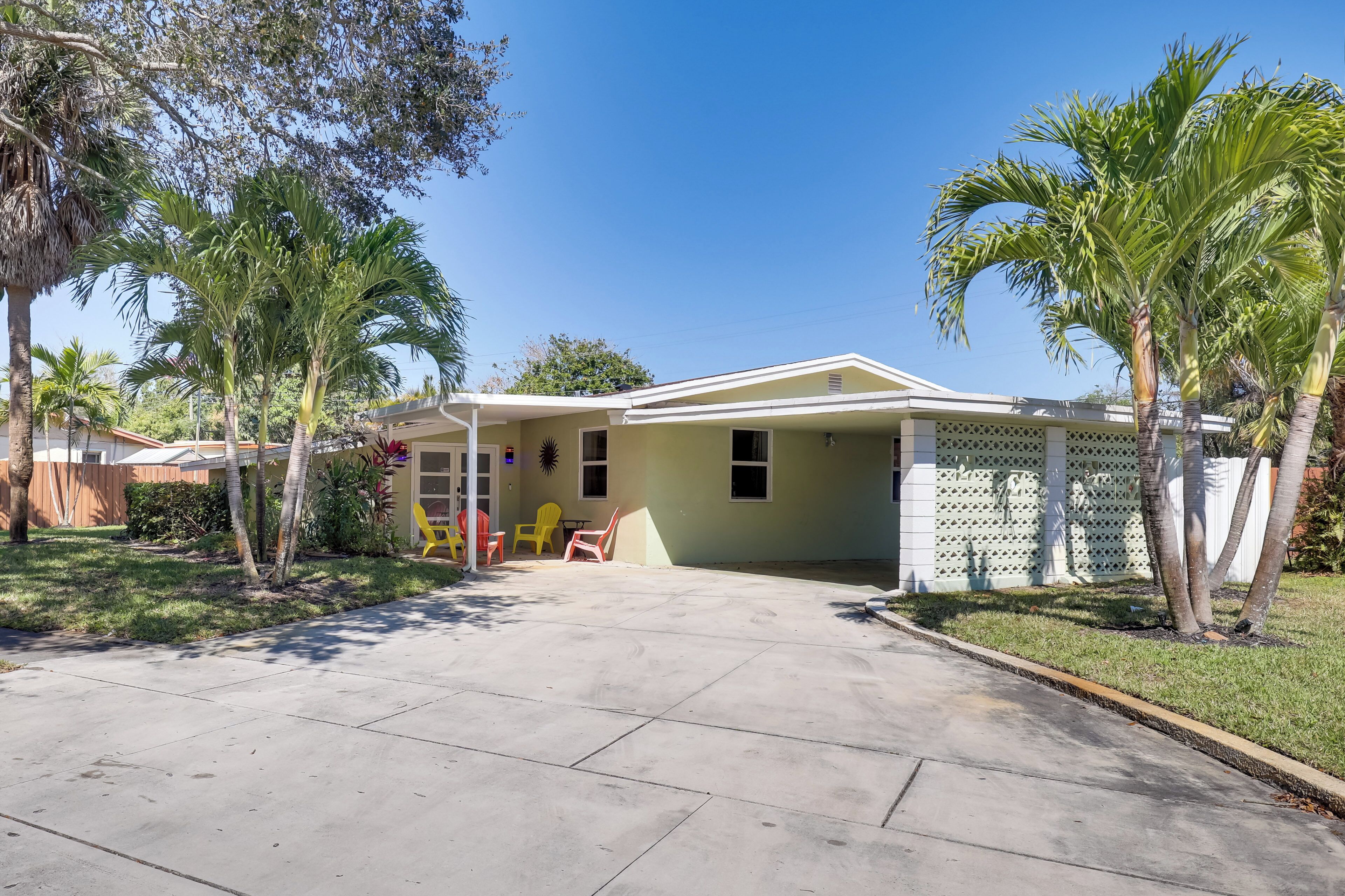 A single-story house with a covered patio, a fenced yard, and palm trees.