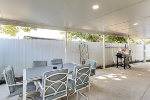 Eine Außenpatio mit Tisch, Stühlen, einem Grill und einem weißen Zaun.