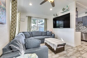 Ein Wohnzimmer mit einer Eckcouch, einem Couchtisch, einem Deckenventilator und einer Küchenzeile mit gefliestem Rücksprühefeld.