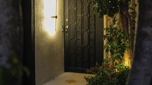 A dark entrance with a lit door, a concrete wall, and a small tree to the right. - House in Merida near Parque de las Americas. (For families and couples) (Mérida)