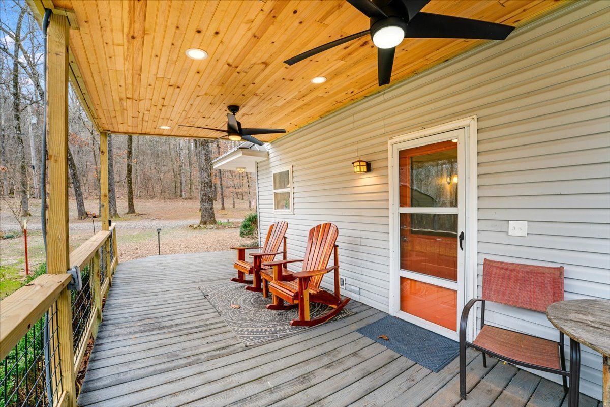 Une terrasse en bois avec des fauteuils à bascule et une table, un ventilateur de plafond et une porte avec des panneaux de verre.