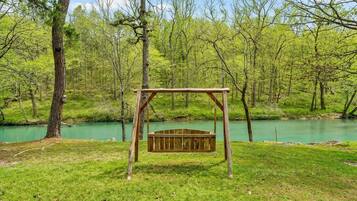 A wooden swing set in a grassy area with a river in the background.