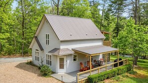 Ein zweistöckiges Haus mit überdachter Veranda, einer Terrasse und einer kleinen Sitzgelegenheit im Freien.
