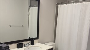 Un baño moderno con un lavabo blanco, muebles oscuros, un espejo grande y un inodoro blanco.