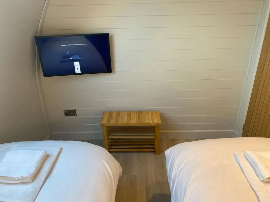 A bedroom with two beds, a TV mounted on the wall, and a small wooden bench.