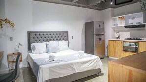 A modern hotel room with a large bed, a built-in wardrobe, a kitchenette, and a small desk area. - 1 Bedroom Apartment Helena + Jacuzzi Medellín (Medellín)