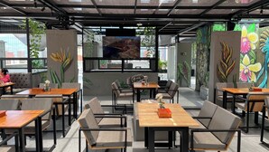 A modern cafe with wooden tables and chairs, large windows, and vibrant wall art. - 1 Bedroom Apartment Helena + Jacuzzi Medellín (Medellín)