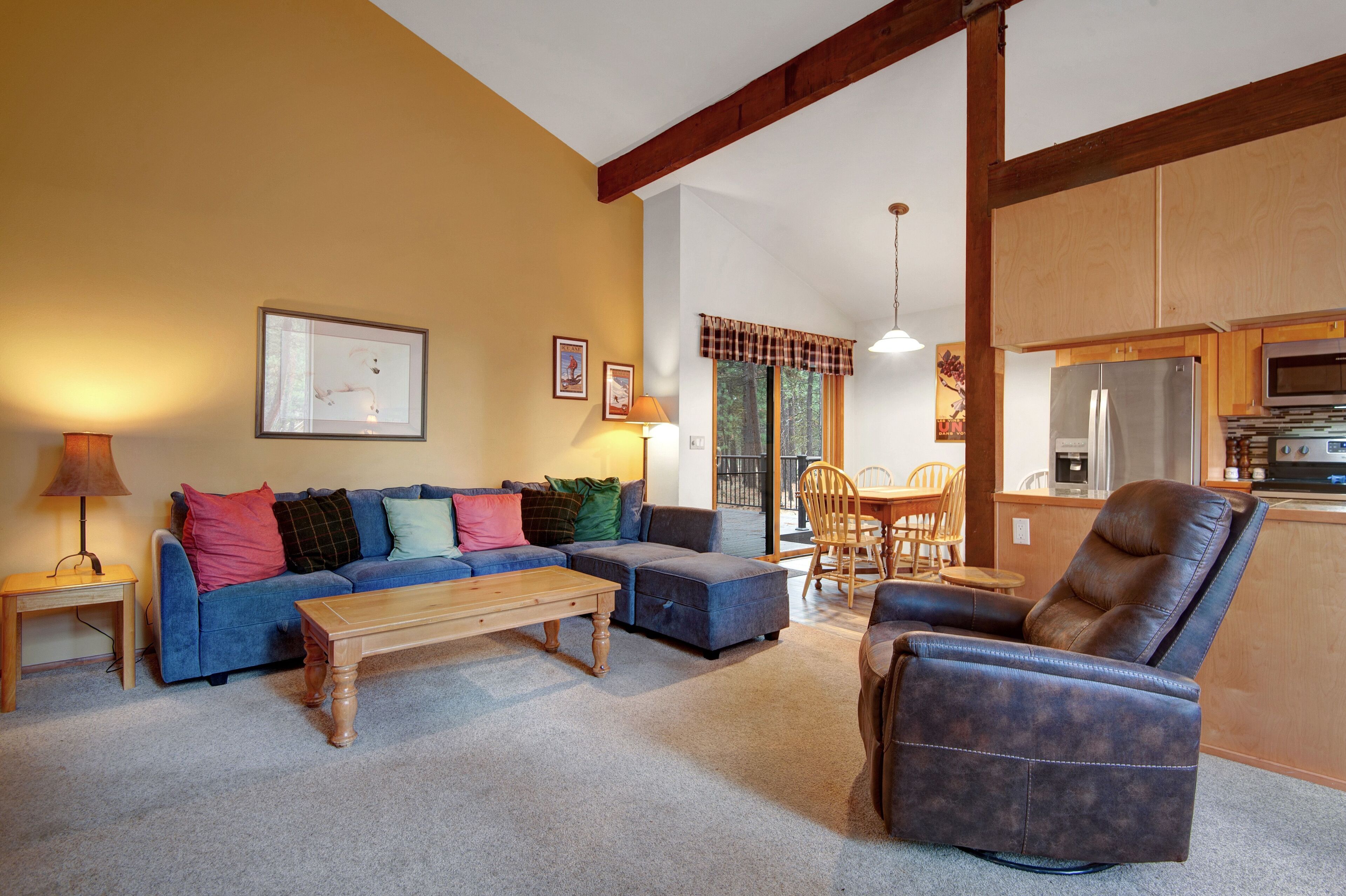 A living room with a sofa, ottoman, and recliner, a wooden coffee table, and a dining area with a table and chairs.