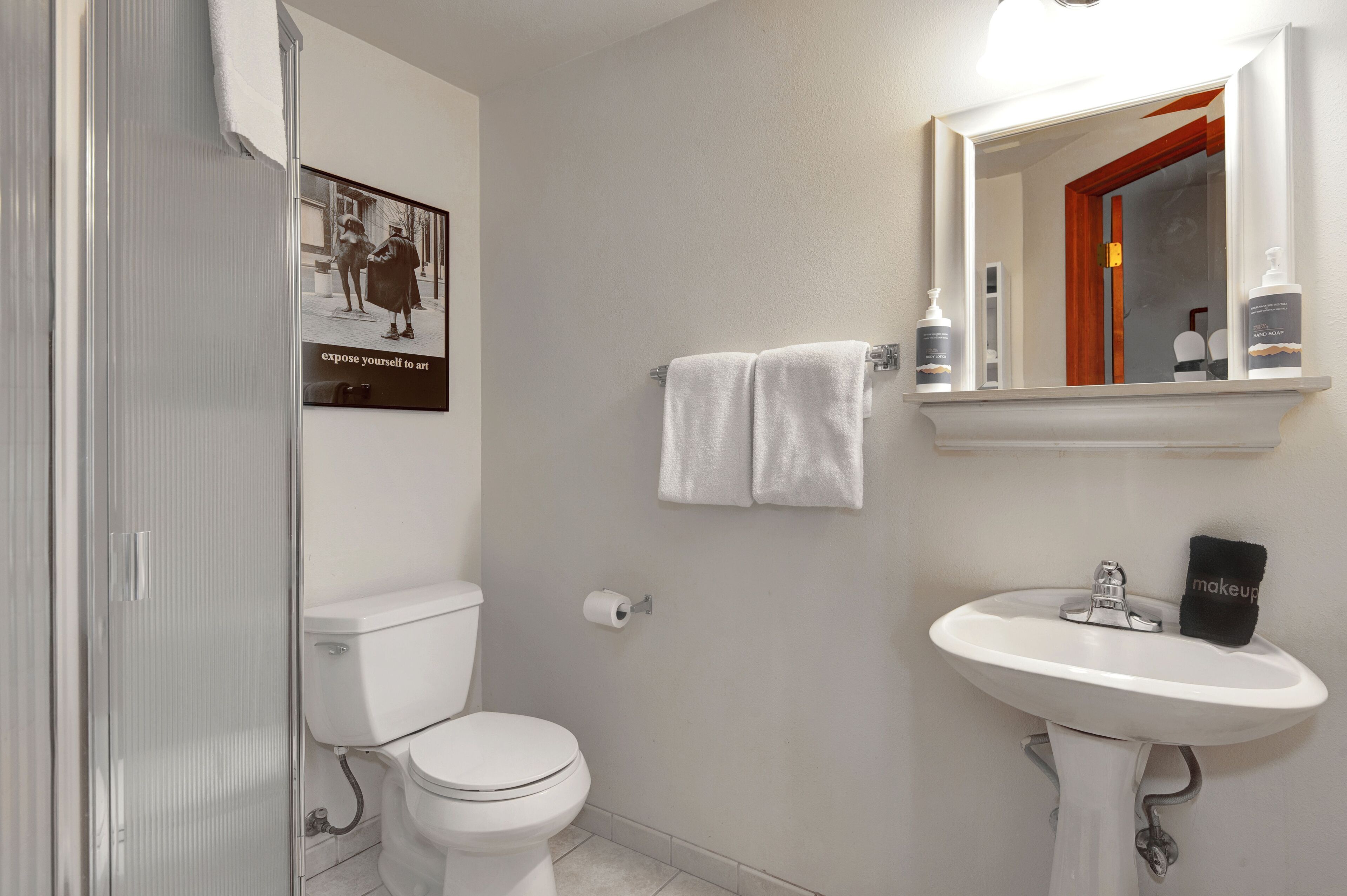 Een badkamer met toilet, wastafel en spiegel boven de wastafel. Een handdoek hangt aan de muur en er is een ingelijste foto.