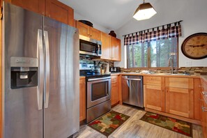 Una cocina moderna con electrodomésticos de acero inoxidable, armarios de madera, un reloj grande y un ventanal con un valance escocés.