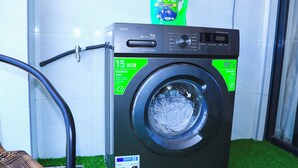 Eine Frontlader-Waschmaschine mit einer Persil-Waschmittel-Flasche darauf, einem digitalen Display und einem 15-Minuten-Waschprogramm-Anzeiger.