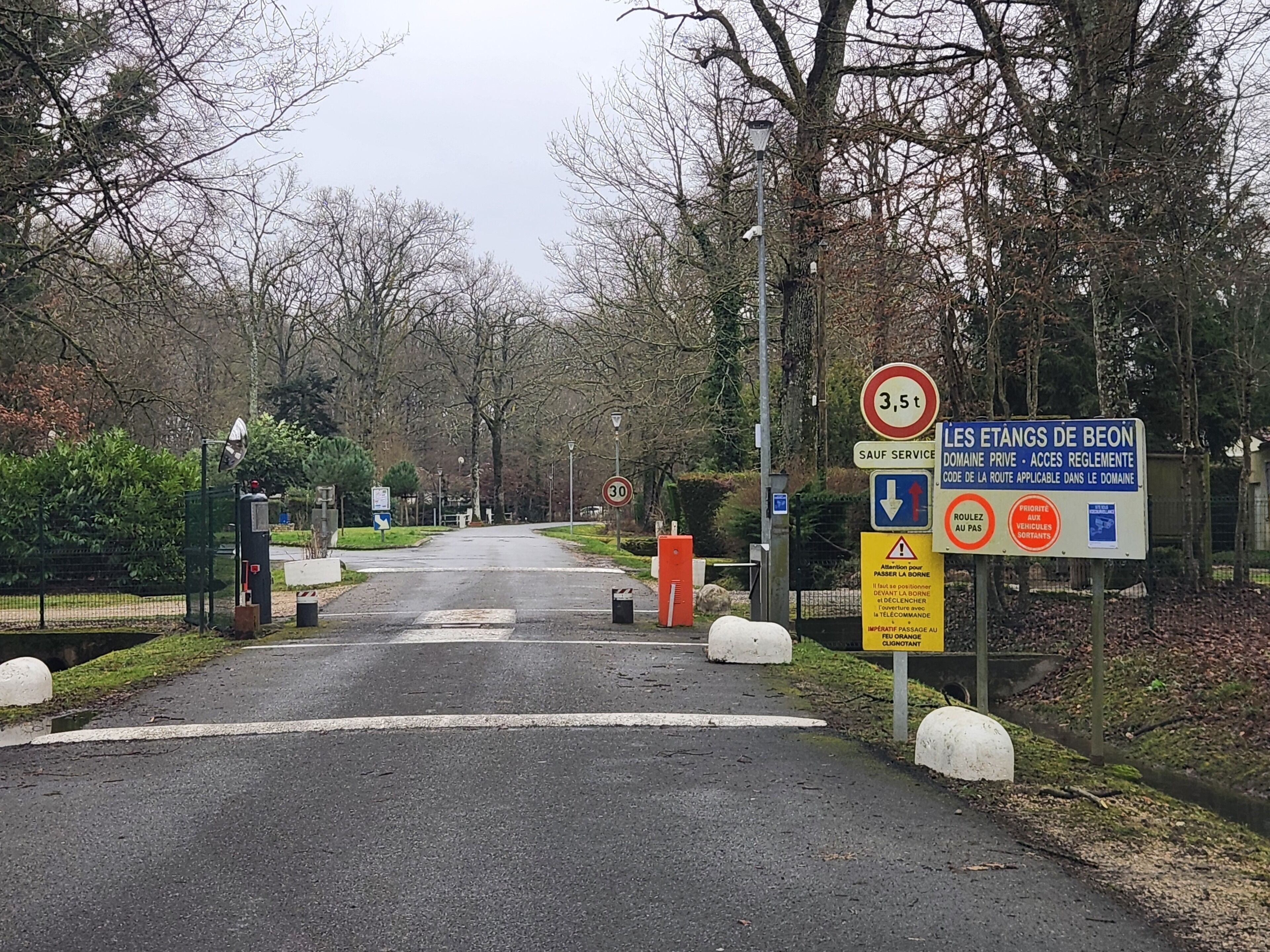 A road leading into a residential area with a speed limit sign of 30 km/h, a sign indicating private domain access, and bollards along the road.