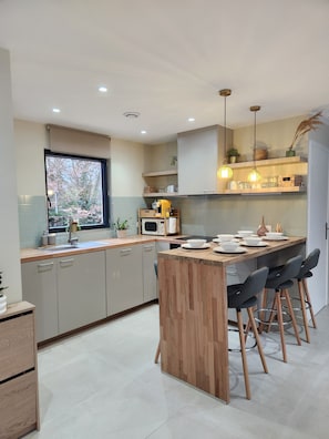 A modern kitchen with a central island, built-in cabinets, and pendant lighting. - House in private domain forest & ponds-ideal family vacation 1h30 from Paris (Bazoches-sur-le-Betz)