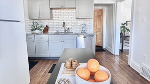 A modern kitchen with white cabinets, a black countertop, and a wooden dining table with a bowl of oranges and decorative items. - Modern Spa Hot Tub Lake Access Clean townhome (Cleveland)