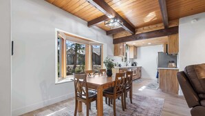 A modern kitchen with wooden cabinets, a central island, and a dining area with a wooden table and chairs. - The Herold's Shaver Lake Retreat | BBQ, Fire pit+ (Shaver Lake)