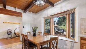 A dining area with a wooden table and chairs, a potted plant, and a view of the outdoors through large windows. - The Herold's Shaver Lake Retreat | BBQ, Fire pit+ (Shaver Lake)