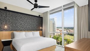 Una camera d'albergo con un letto grande, una ventola a soffitto, vista sulla città e un'ampia finestra.