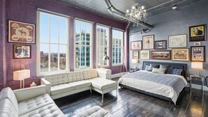 A modern bedroom with a large bed, a sofa, and a view of the city through large windows. - Luxury Penthouse Near Yum Center + Parking
  (Louisville)