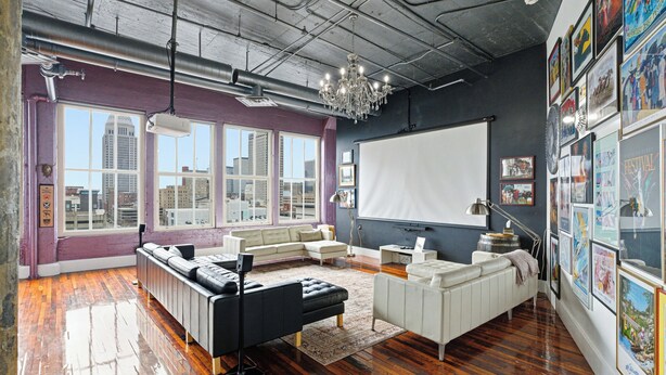 A spacious living room with a large window, a projector screen, and a collection of framed artwork on the walls. - Luxury Penthouse Near Yum Center + Parking
  (Louisville)