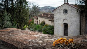 Un edificio de piedra con un campanario, rodeado de vegetación y colinas al fondo.