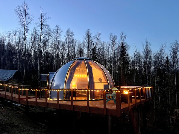 A dome-shaped structure with a wooden deck, surrounded by trees. - Aurora Igloo w/ Hot Tub & Firepit near town. (Fairbanks)