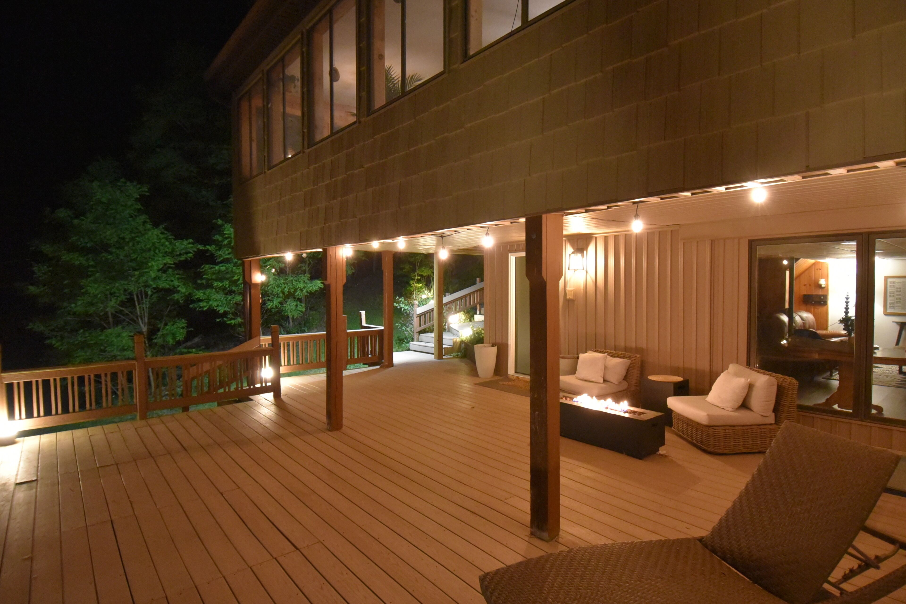 Una terraza de madera con mobiliario exterior y un ventanal que da a un espacio interior.