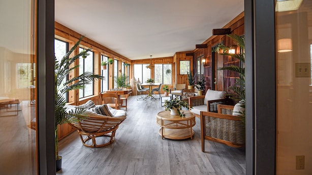 Quarto amplo com piso de madeira, móveis de vime e grandes janelas que permitem a entrada de luz natural.